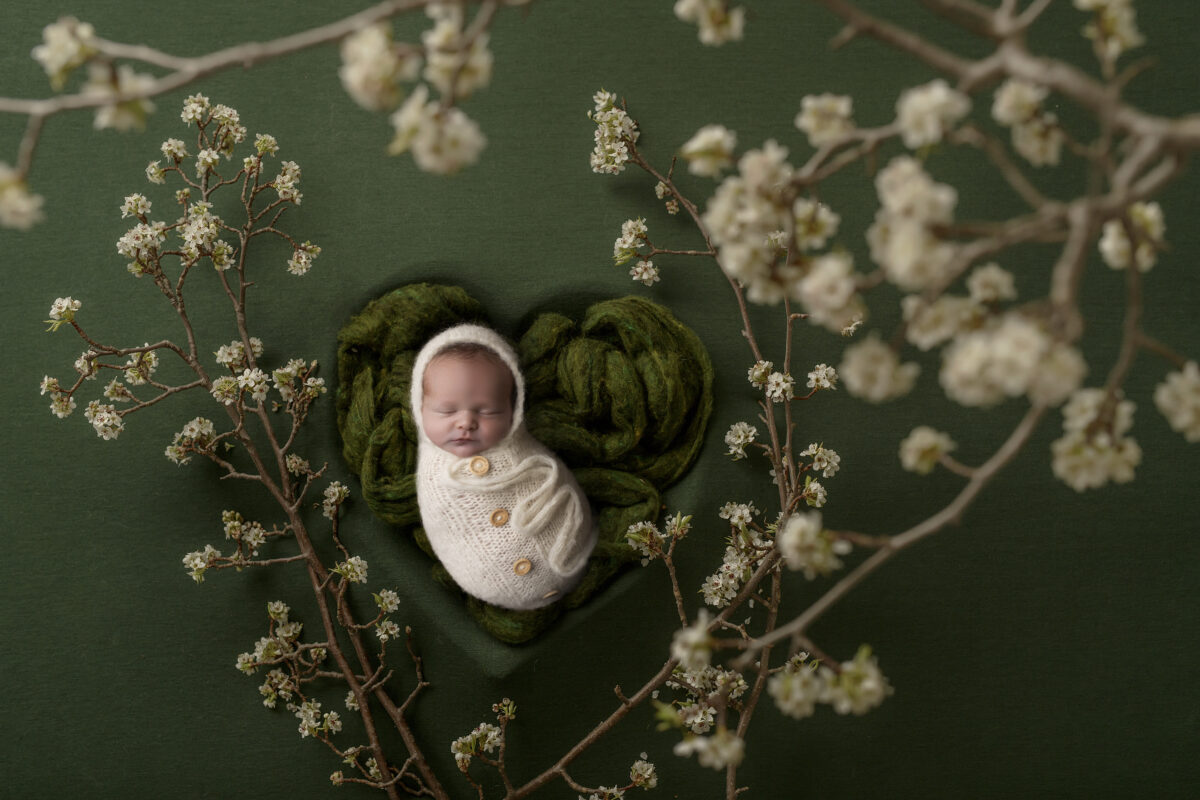 newborn baby with white flowers and white wrap with buttons in green heart during her photoshoot at Kristy’s Studio, Wentworth Falls.