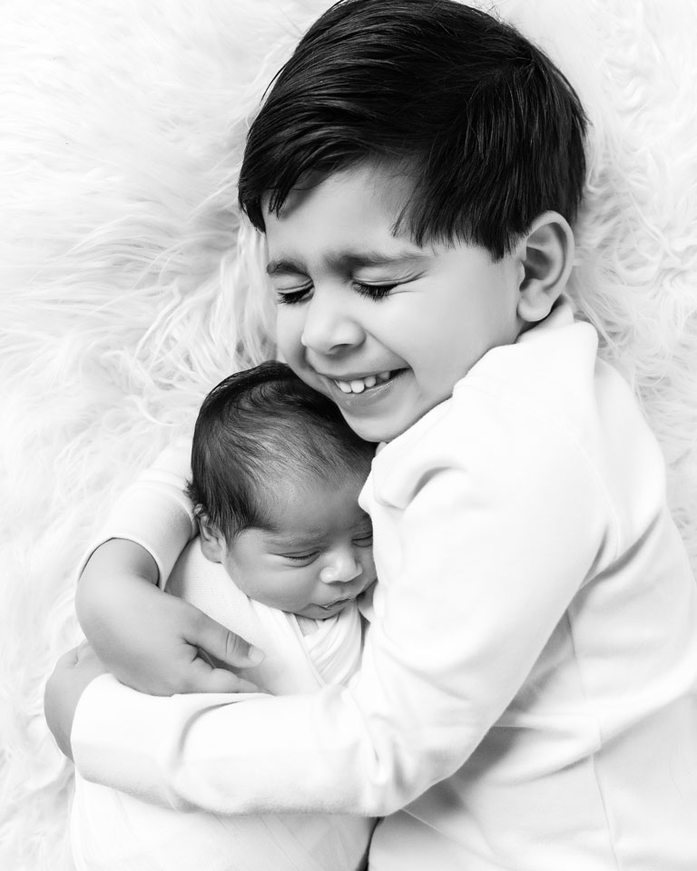 little boy cuddling and smiling with newborn baby black and white portrait at Kristy’s Studio, Blue Mountains — relaxed, joyful moment